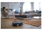 Aspirateur robot sur parquet dans un salon avec une femme lisant en arrière-plan.