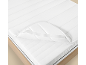 Protège-matelas blanc et matelas sur un cadre de lit en bois.
