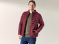 Un homme porte une veste matelassée rouge et un jean.