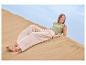 Femme en haut vert et pantalon beige se relaxant sur une dune de sable.
