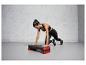 Une femme fait des exercices avec une plateforme de step rouge et noire.