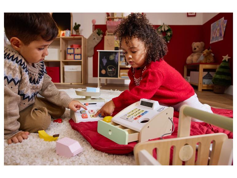 Deux enfants jouent avec une caisse enregistreuse et une balance jouets sur un tapis.