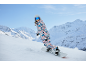 Femme en combinaison de snowboard colorée et casque faisant du snowboard en montagne.