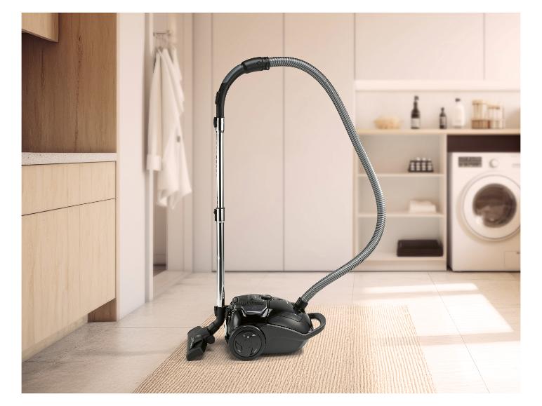 Aspirateur noir sur un tapis dans une buanderie avec des armoires en bois et une machine à laver.