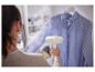 Une femme repasse une chemise à rayures avec un fer à repasser vapeur.