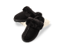 Pantoufles noires en fausse fourrure sur un cube blanc.