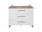 Commode blanche à trois tiroirs et poignées en bois, avec pieds coniques et plateau en bois.