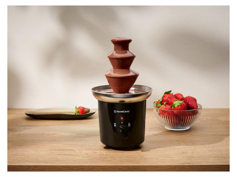 Fontaine à chocolat noire avec des fraises fraîches sur une table en bois.