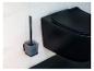 Une brosse de toilette noire et son support sont fixés à un mur carrelé gris clair à côté de toilettes noires.