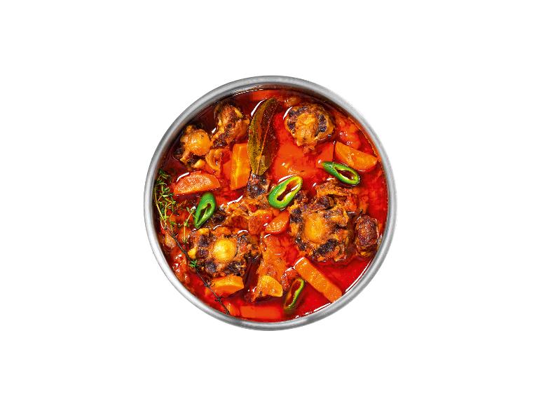 Une casserole avec du bœuf, des carottes et des poivrons verts dans une sauce rouge.