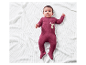 Bébé dans une grenouillère rouge à motif lapin sur une couverture blanche.