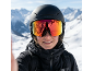 Femme avec un casque de ski noir et des lunettes de ski à verres réfléchissants en montagne enneigée.