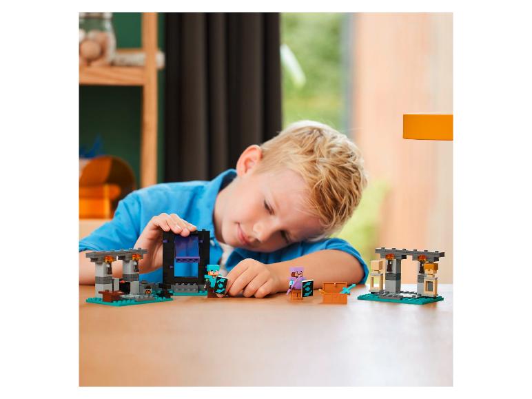 Un enfant joue avec un set LEGO Minecraft avec un portail du Nether et des figurines.