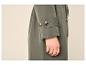 Manche de manteau vert kaki avec des boutons et une main portant des bagues dorées.
