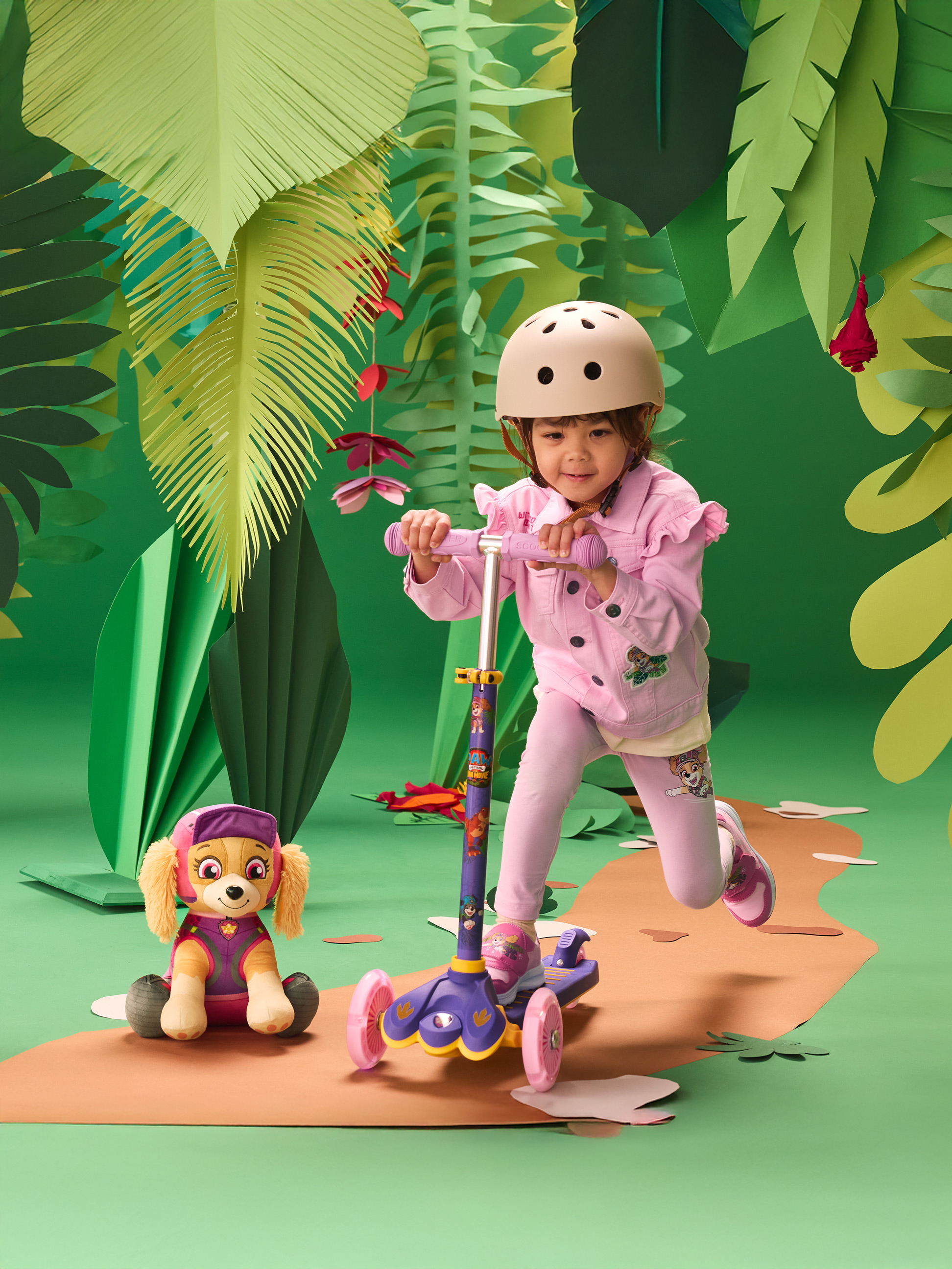 Fille en casque sur trottinette, avec une peluche, dans un décor de jungle.