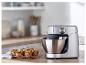 Robot de cuisine argenté avec bol en acier inoxydable et muffins sur une table en bois.