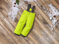 Pantalon de ski jaune avec bretelles sur un plancher en bois avec de la neige.