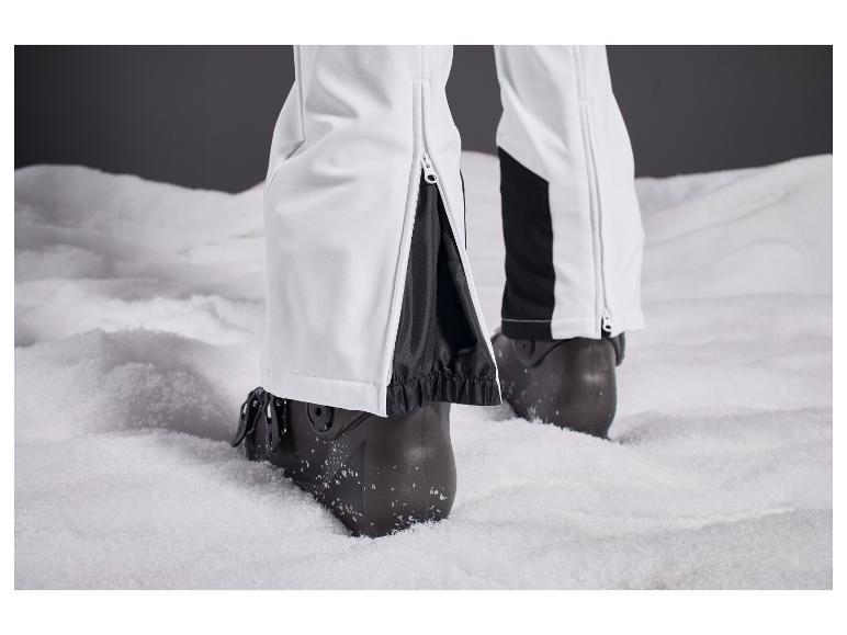 Pantalon de ski blanc avec des inserts noirs et des chaussures de ski noires dans la neige.