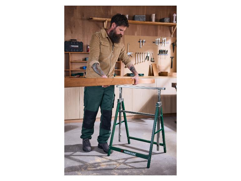 Homme plaçant une planche de bois sur des tréteaux dans un atelier.