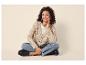 Femme en cardigan tricoté beige, jean et mocassins noirs, assise en tailleur.