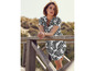 Femme en robe blanche à imprimé de feuilles noires, appuyée sur une balustrade en bois.
