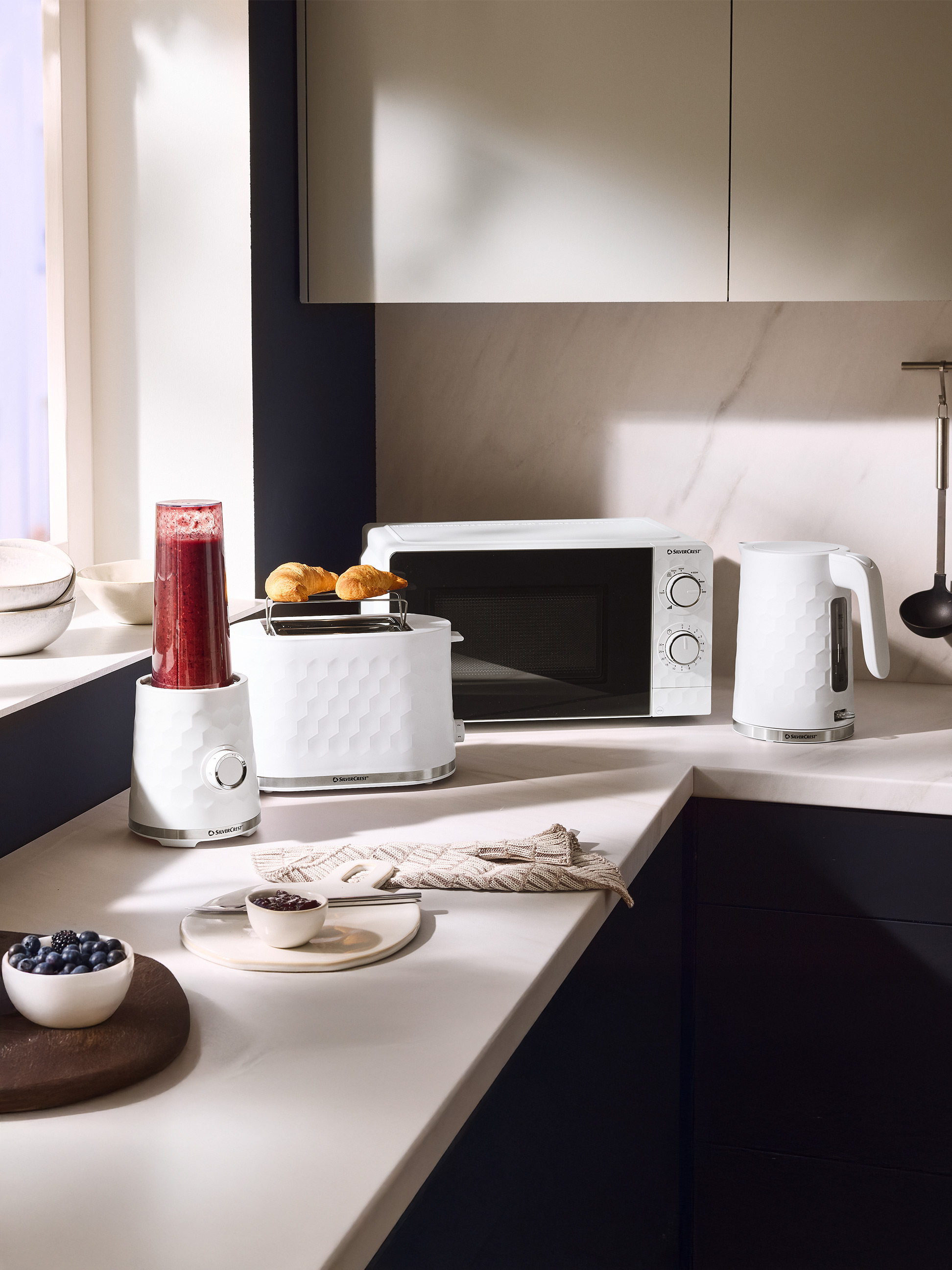 Appareils de cuisine blancs : mixeur, grille-pain avec croissants, micro-ondes et bouilloire.