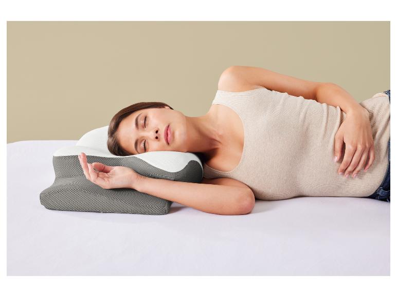 Femme dormant sur le côté sur un lit avec un oreiller ergonomique gris et blanc.