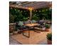Salon de jardin avec table en bois, canapés gris foncé et guirlandes lumineuses sous une pergola.