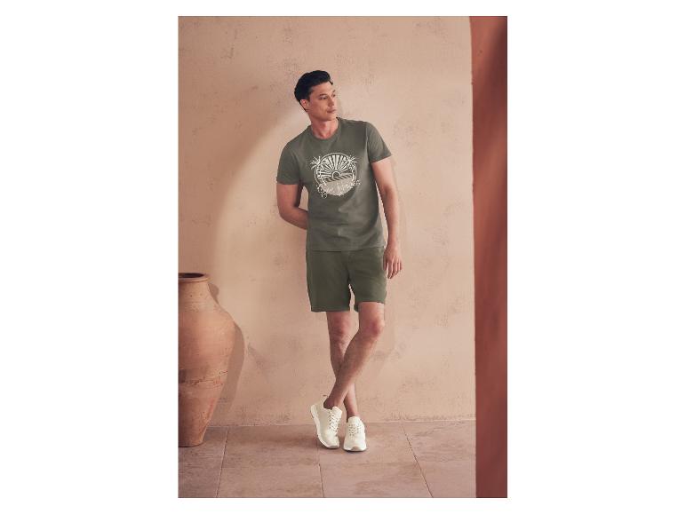 Un homme modèle un t-shirt et un short verts, avec des baskets blanches.