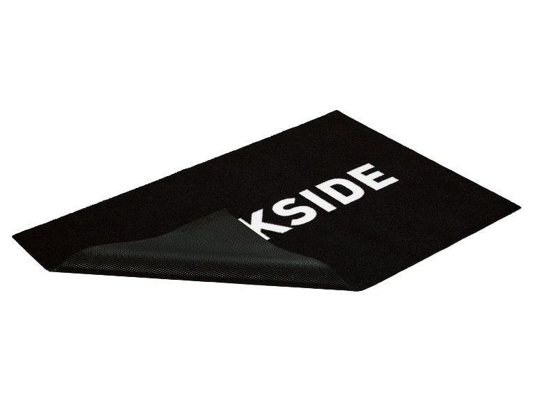 Un paillasson noir KSIDE avec inscription blanche, partiellement roulé.