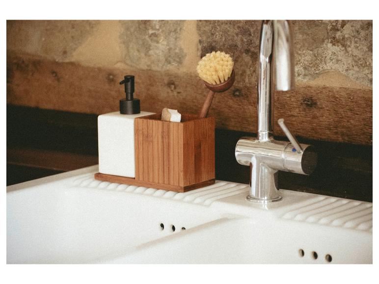 Distributeur de savon et brosse à vaisselle dans un organiseur en bambou dans une cuisine rustique.