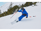 Enfant skie en tenue de ski bleue, avec skis, bâtons, casque et lunettes sur montagne enneigée.