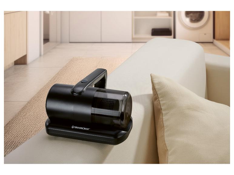 Aspirateur à main noir sur un canapé clair avec un coussin dans un salon.