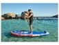 Homme faisant du paddleboard sur eau claire, gilet de sauvetage, rochers en arrière-plan.