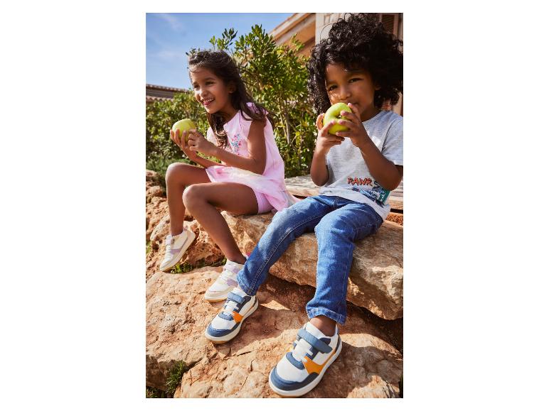 Deux enfants en jean et en baskets mangent une pomme à l'extérieur.