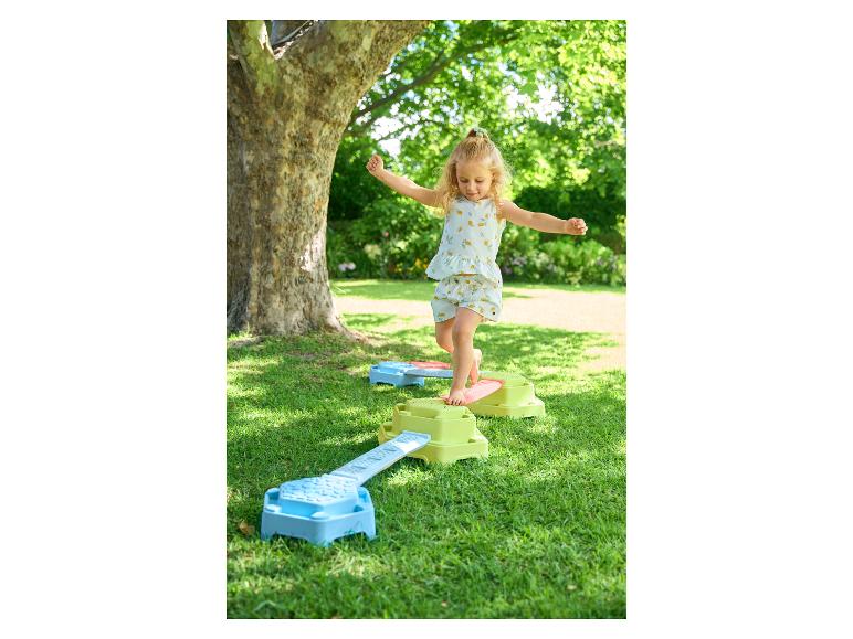 Une enfant joue sur des blocs d'équilibre colorés en extérieur.