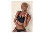 Femme souriante aux cheveux blonds courts, main sur le menton, portant un soutien-gorge et une culotte noirs.