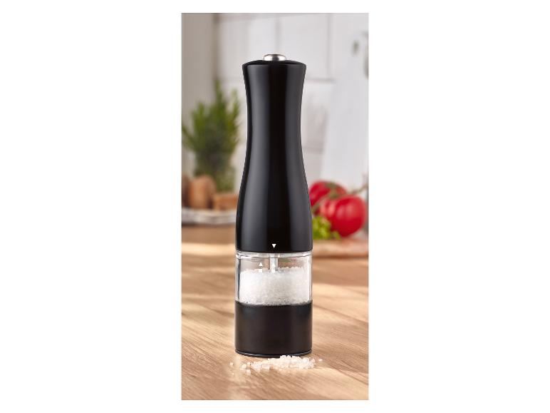 Moulin à sel ou à poivre noir sur une table en bois avec des tomates en arrière-plan.