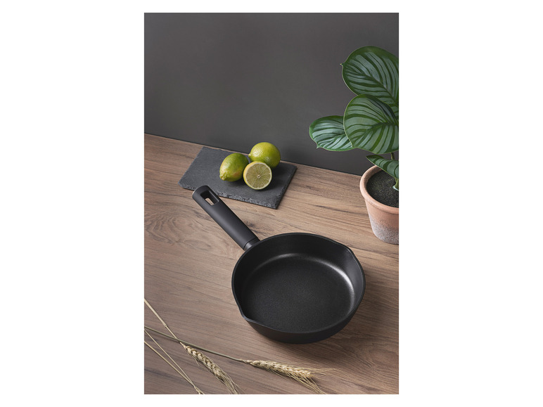 Une poêle noire sur une table en bois avec des citrons et une plante.