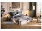 Chambre avec literie grise, lit beige, pouf et parquet en bois.