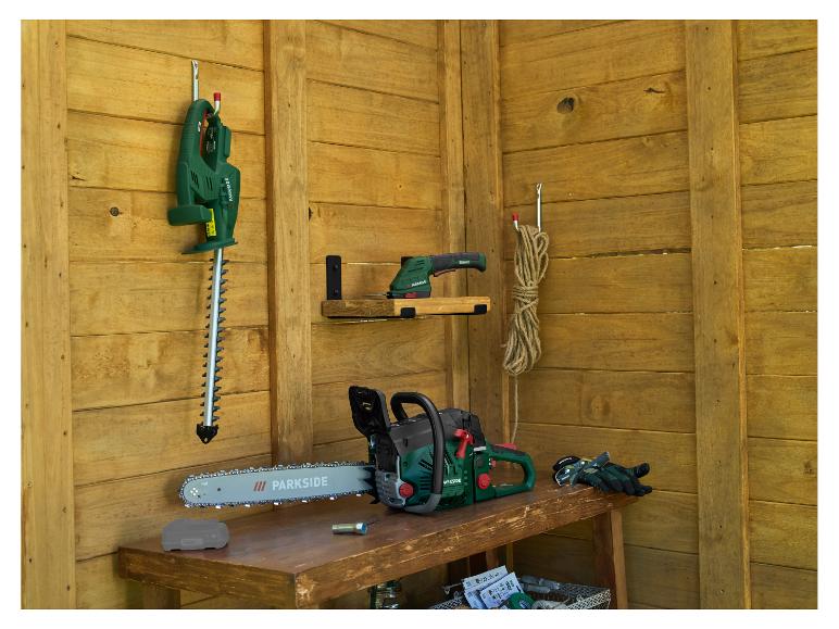 Outils de jardin dans un abri en bois : tronçonneuse, taille-haie et ponceuse vibrante.