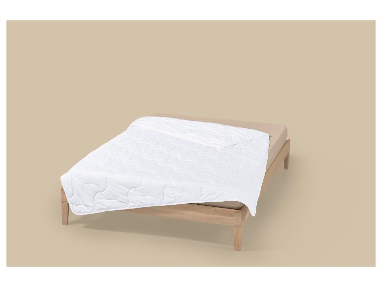 Couette blanche sur un lit en bois avec des draps beiges.
