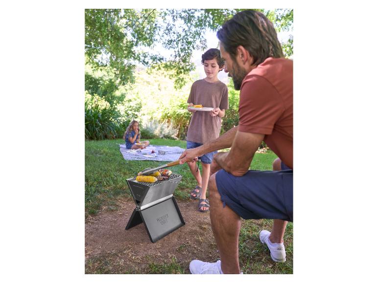 Père et fils font un barbecue portable, une fille assise sur une couverture en arrière-plan.