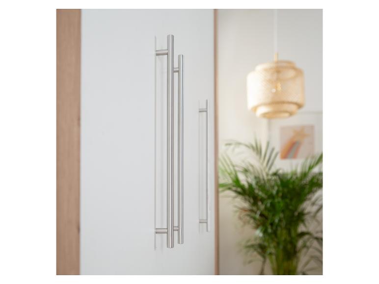 Portes d'armoire blanches avec de longues poignées métalliques fines dans une pièce lumineuse avec une lampe suspendue et une plante.