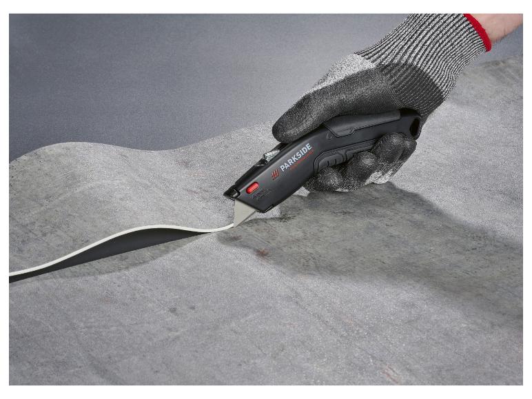 Une main gantée utilise un cutter Parkside pour couper un matériau.