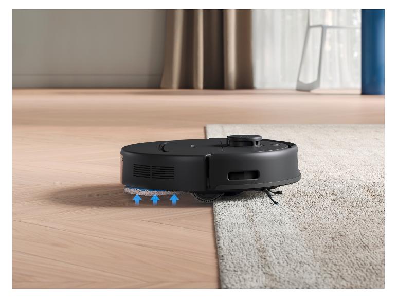 Un aspirateur robot noir passe d'un parquet en bois à un tapis clair.