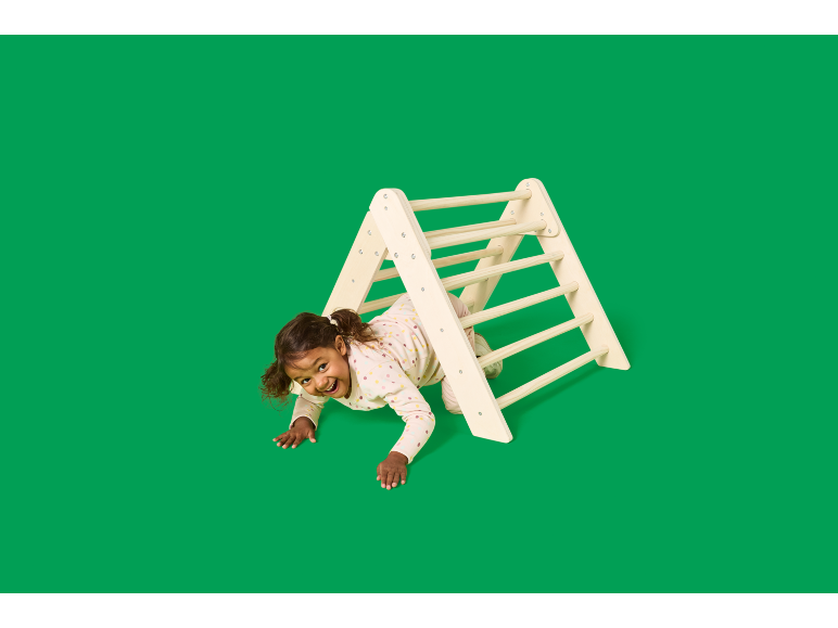Enfant joyeux rampant à travers un triangle d'escalade en bois.