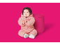 Bébé joyeux en combinaison de neige rose matelassée, applaudissant à côté d'un pouf rose.