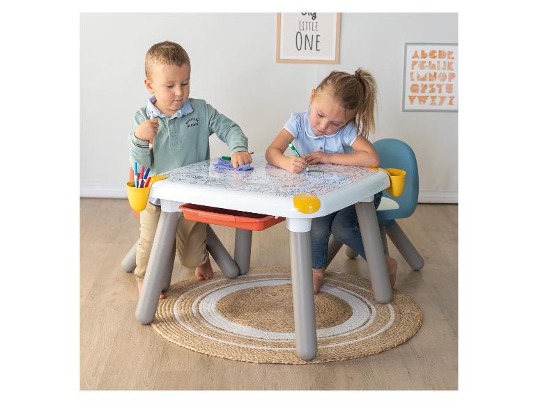 Deux enfants dessinent à une table blanche avec rangements et marqueurs.