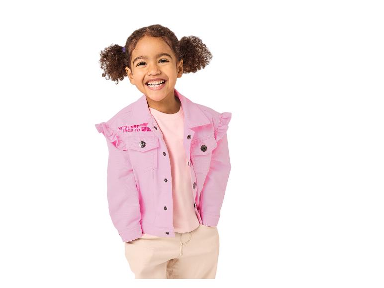 Fille souriante en veste en jean rose à volants et pantalon beige.